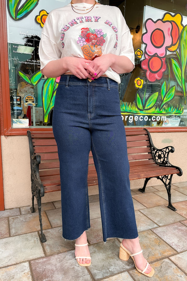 Close up of a woman wearing a graphic tee shirt with dark wash super high rise culotte pants and woven heels.