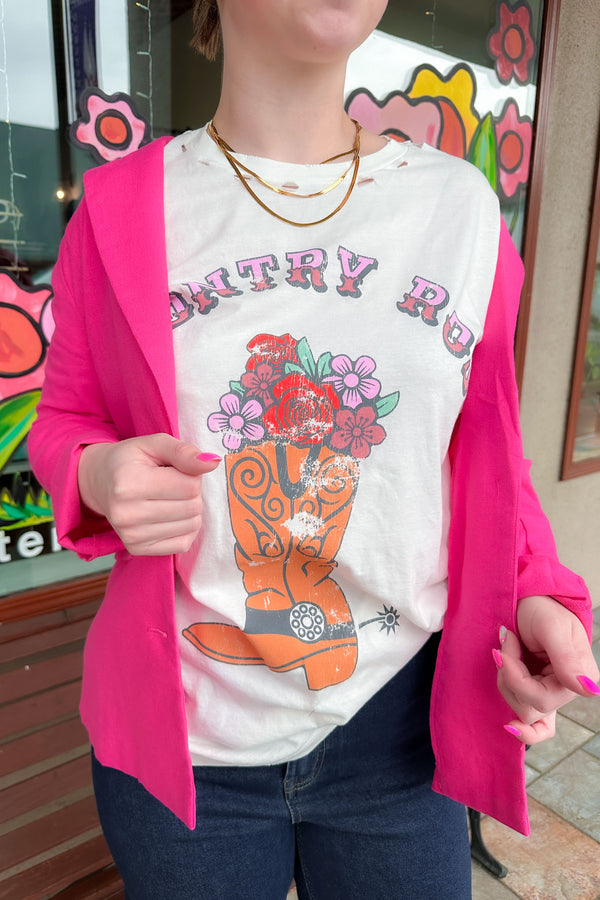 Woman wearing a country rose graphic tee shirt under a bright pink blazer with dark denim jeans.