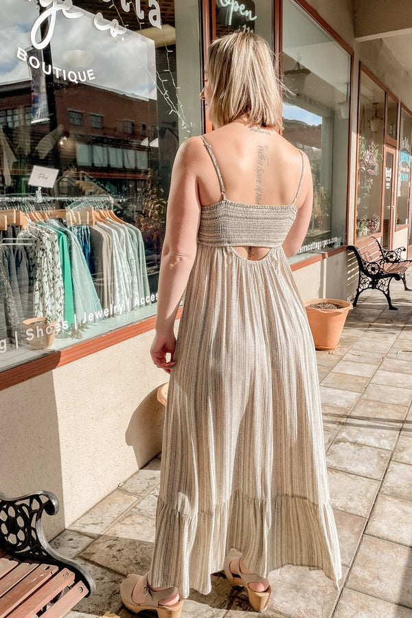 Blonde girl wearing a black and cream striped maxi dress. (Back view)
