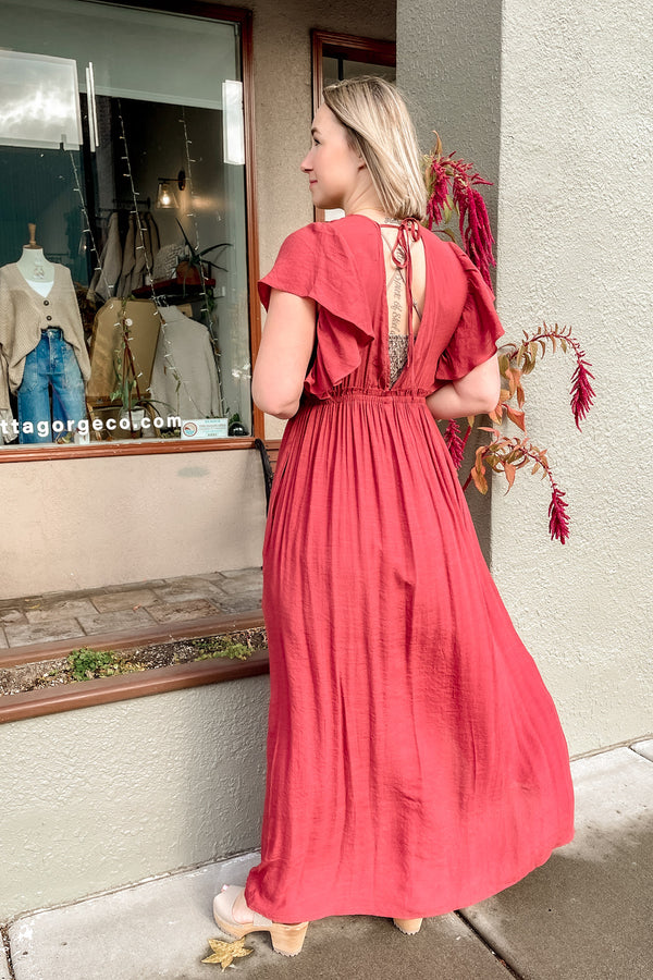 Blonde girl wearing a sienna colored maxi dress with clogs. (Back view)
