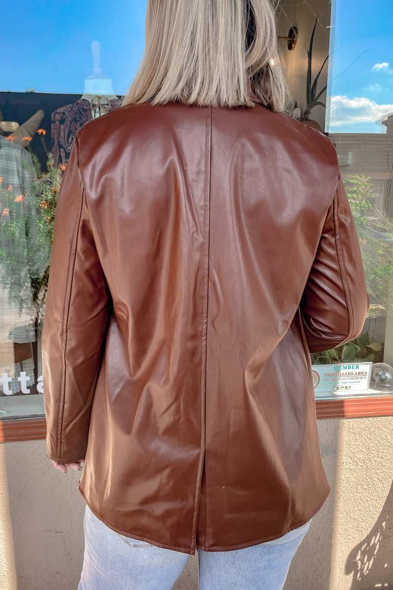 Blonde girl wearing a chocolate brown faux leather jacket with jeans showing off the back of the jacket wearing jeans