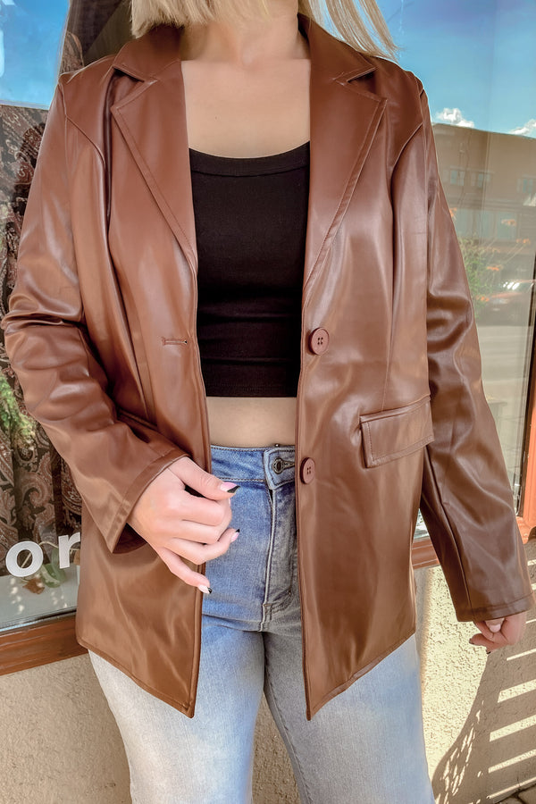 Blonde girl wearing a chocolate brown faux leather jacket over a black cropped shirt with jeans 